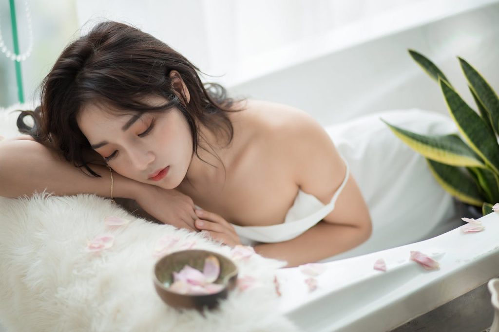 A serene moment of relaxation in a bathtub surrounded by rose petals and plush textures.