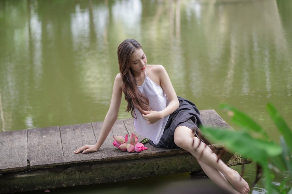 Young woman posing on a wooden pier by a lake with flowers, exuding tranquility and summer vibes.